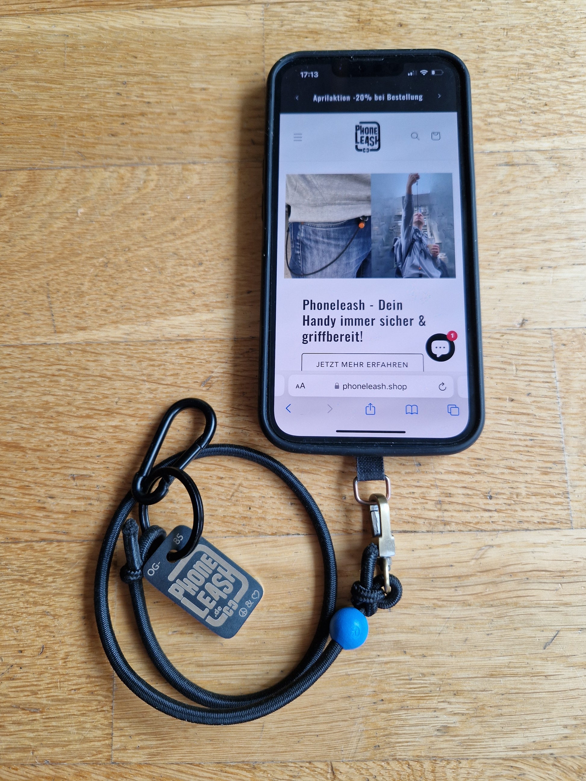 Original Phoneleash Schwarz Blau Handykette mit elastischem Band für sicheren, stilvollen Smartphone-Gebrauch. In Deutschland gefertigt, bietet sie Langlebigkeit und ein dezentes Design mit einer Friedensbotschaft durch ein handgestanztes Peace-Zeichen und Herz. Darstellung mit Handy